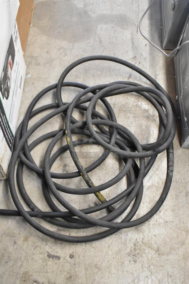 Coiled black hoses on a concrete floor, showing signs of wear. Auction item: 2 hoses. 2 times your bid.