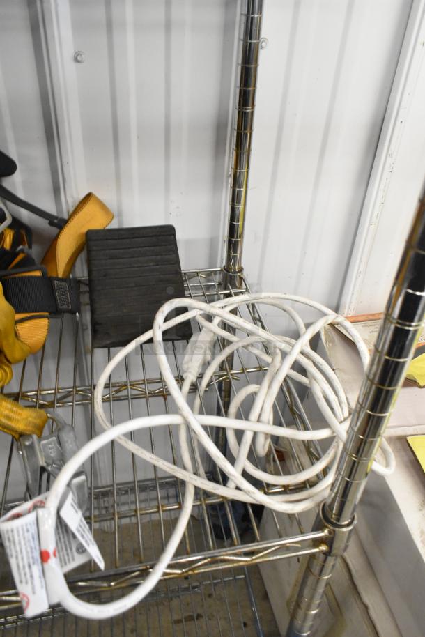 Metal tiered shelf holding various items including a black rubber block, white power strip, yellow safety strap with clips.