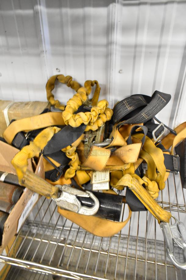 A lot of various items including yellow and black straps with hooks, metal rods, and stands on a metal shelf.