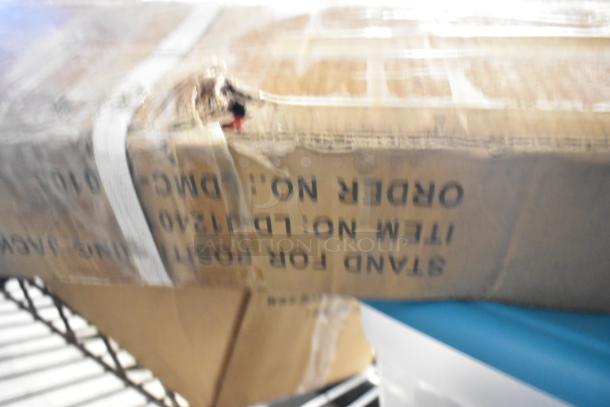 Cardboard box with "ITEM NO: LD112540" printed, containing a tier lot of various items including a stand, metal pieces, and a strap. Box shows signs of wear.