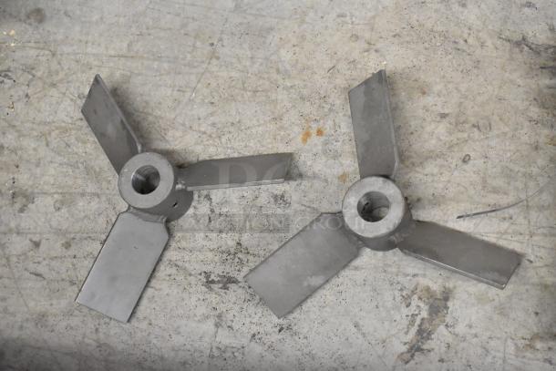 Two metal propeller-like parts, possibly from Prince RD-150-16 or RD522CCAA5A4B1, on a concrete surface.