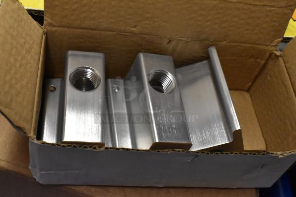 Cardboard box containing metal components with threaded holes, indicating use in assembly or fittings.