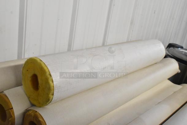 Lot of insulation rolls with fiberglass cores and white outer covering, stacked against a metal wall.
