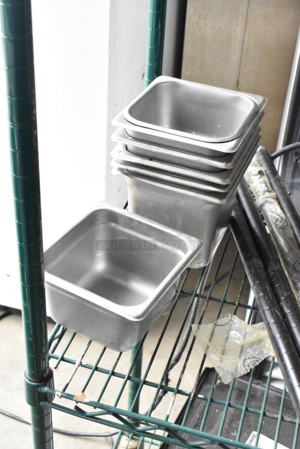 Lot of stainless steel drop-in bins stacked on a metal shelving unit alongside metal rods, in used condition.