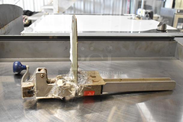 Brand new Edlund 905 metal commercial can opener with mount, slight scratches, blue handle, wrapped in plastic, on steel surface.