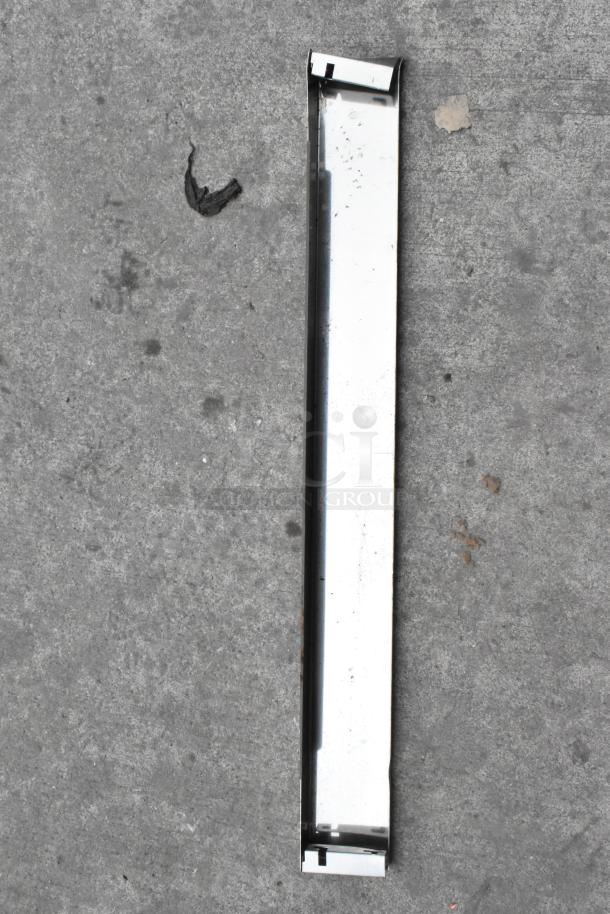 A metal component lying on a concrete surface, possibly a part of the Cooking Performance Group flat top griddle setup.
