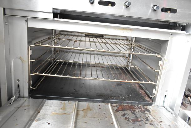 Cooking Performance Group stainless steel gas flat top griddle with oven, overshelf, backsplash, on casters. Visible wear.