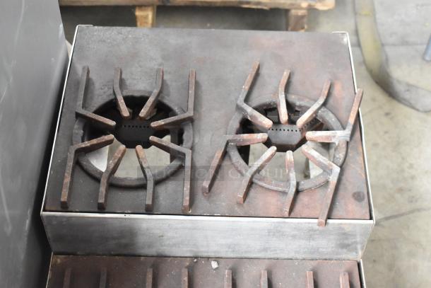 Metal commercial countertop gas range with four burners and two tiers. Shows signs of wear. Ideal for high-demand kitchens.