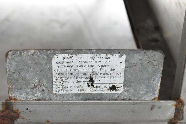 Metal commercial countertop gas-powered 4 burner 2 tier range, used condition, worn label with maintenance instructions visible.