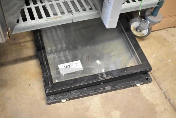 Two merchandiser doors stacked on the floor, each with a black frame and clear glass. Label indicates "162 QTY x2".