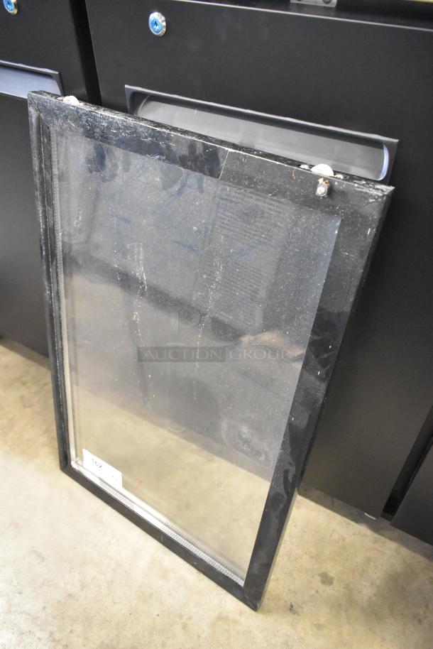Clear glass merchandiser door with black frame, slight dust marks. Tag reads "162." Intended for display coolers.