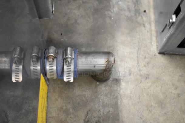 Stainless steel pipe section with hose clamps connected to a commercial kitchen appliance, possibly for steam or water.