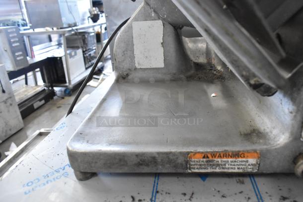 Hobart 1612 stainless steel meat slicer in fair condition. Features 115 volts, 1 phase. Visible wear and a warning label.
