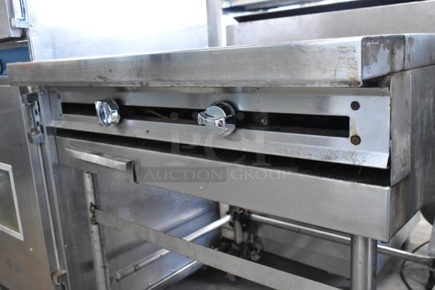 Stainless steel commercial gas griddle with flat top. Features chrome knobs, visible wear, on commercial casters.
