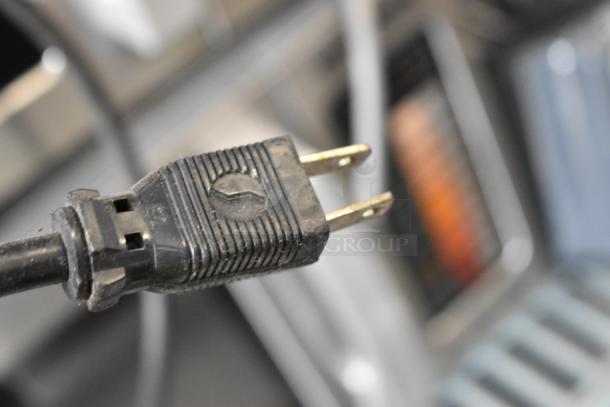 Close-up of a power plug for a DeLonghi Stainless Steel Countertop Automatic Coffee Maker. Plug shows standard prongs.