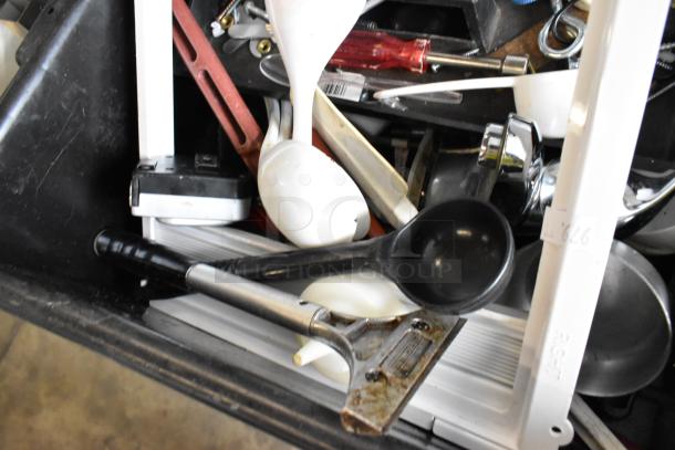 Various utensils and tools in a black poly bus bin, featuring ladles, spatulas, and screwdrivers. Mixed condition.