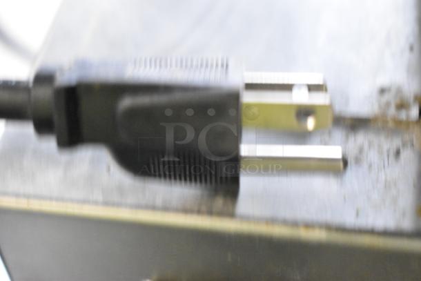 Blurry close-up of an electrical plug on a Avantco 177QS1800SS stainless steel countertop steamer.
