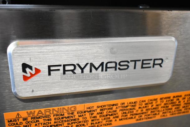 Frymaster stainless steel fryer frame with logo, mounted on commercial casters. Warning label visible below.