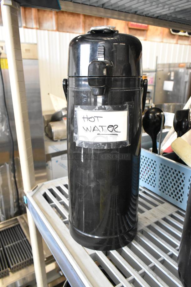Black air pot labeled "HOT WATER" on a metal shelf, used condition. Set of 2, perfect for keeping beverages warm.