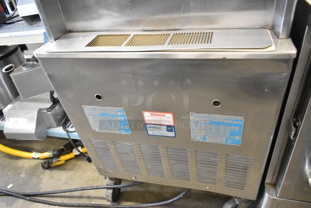 Taylor 339-27 stainless steel two-flavor soft serve ice cream machine on casters. Features air cooling, 208-230V, 1 phase. Tags show model and caution info.