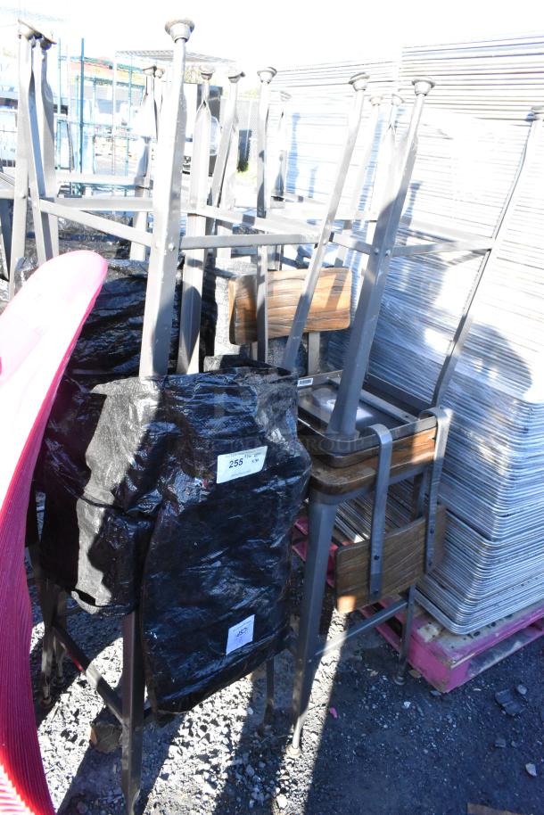 30 metal bar-height chairs with wooden backrests and seats, stacked outdoors. Includes a bid tag.