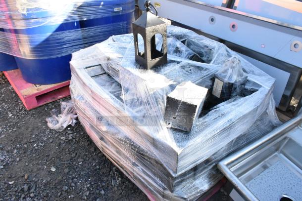 35 black wrought iron metal lanterns wrapped in plastic on a pallet, showing durable construction and rustic design.