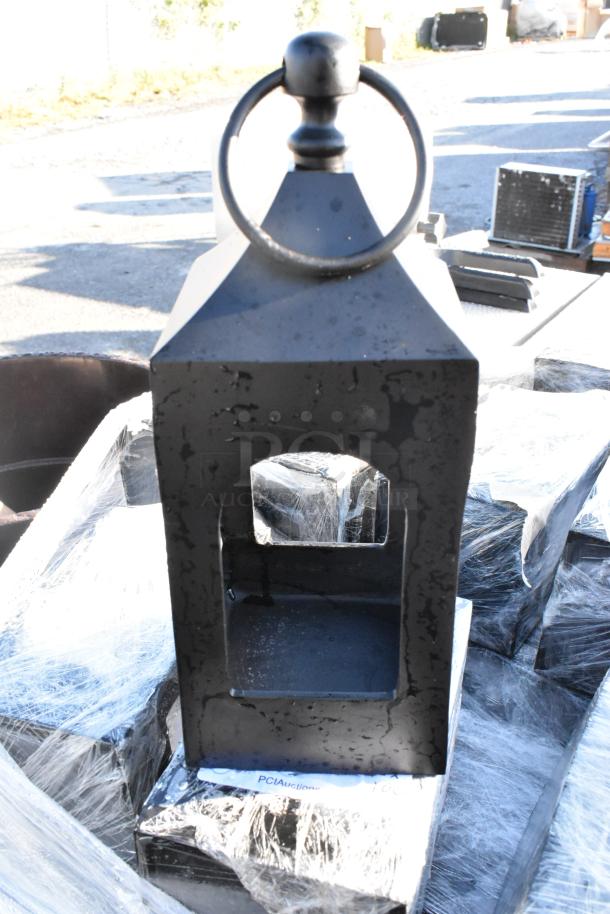Black wrought iron metal lantern, rustic finish, large ring on top. Appears in new condition, stacked with similar lanterns.