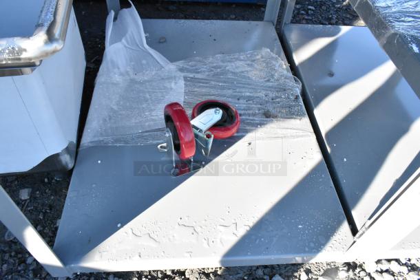 Brand new gray metal 2-tier cart with commercial red casters. Slight scratches visible. Wrapped in protective plastic.