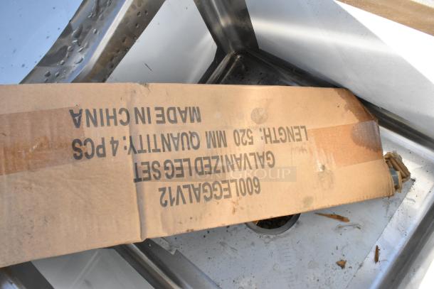 Brand new Regency 600S2171718L stainless steel 2 bay sink with left side drain board, minor scratches and dents, cardboard packaging visible.