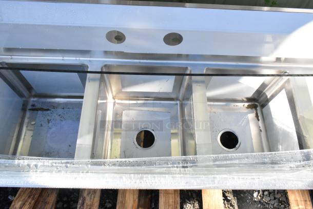 Brand new Regency 600S31416212 stainless steel 3-bay sink with dual drain boards, no legs, visible scratches and dents.