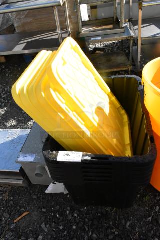 6 brand new black poly bins with yellow lids, scratch and dent condition, multiple auction tags visible.