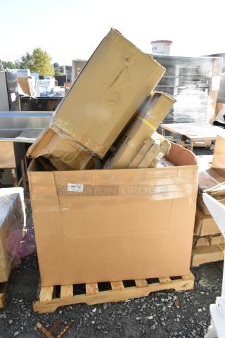 Cardboard box on pallet containing 7 new scratch and dent items, including tabletops and a wire rack, with visible wear.