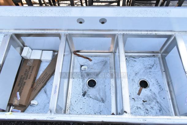 Brand new Regency 600S32030224 stainless steel 3-bay sink with dual drain boards, visible scratch and dent marks.