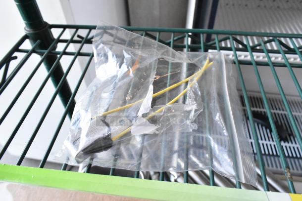 Clear plastic bag containing a small unit with yellow wires and a metal tip on a green wire shelf.