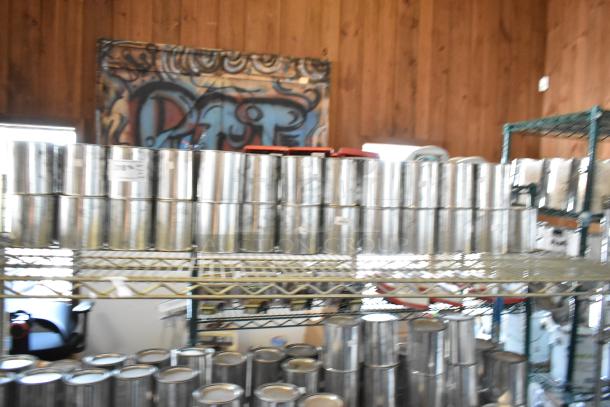 49 Pro Guard chemical cans stacked on a metal shelf, indicating a bulk auction lot. Cans appear metallic and unlabeled.