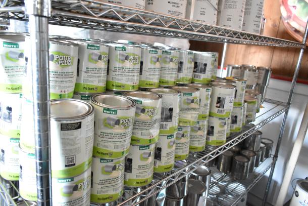 143 Pro Guard chemicals, including White Pour N Plug cans, displayed on shelving. Marked as moisture curing leak stopper.