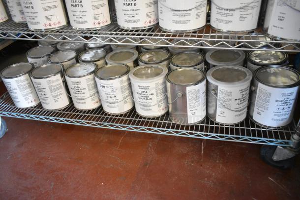 34 Pro Guard chemical cans, including 2114 Moisture Cure Primer Clear Blue, on metal shelves, clean labels visible.