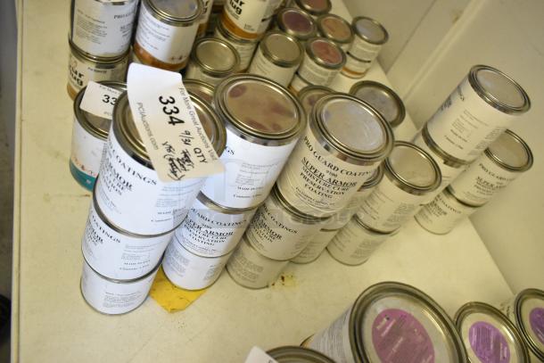18 cans of Pro Guard chemicals, including 9100 Super Armor Moisture Cure Coating, stacked on a shelf. Auction tag visible.