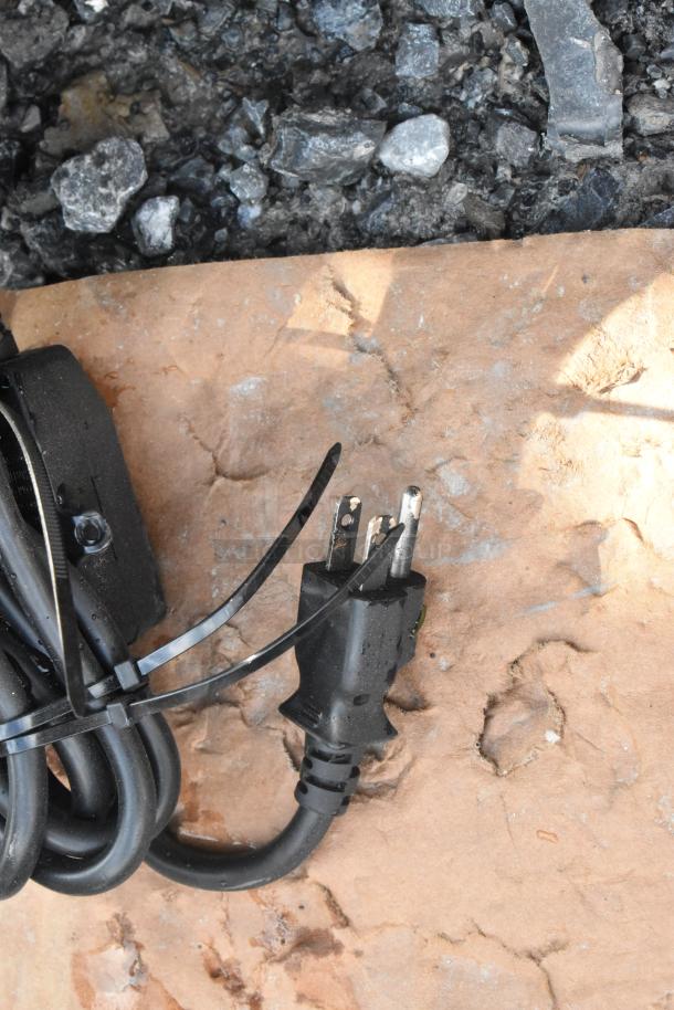 A close-up of a power cord with zip ties on rocky ground, unrelated to the KoolMore KM-VMNT-50-BR vending machine.