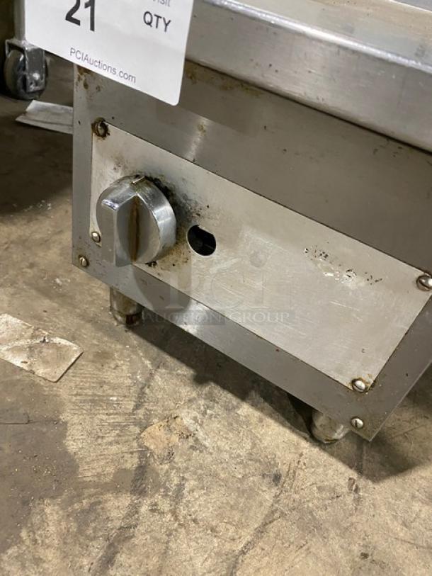 Commercial stainless steel natural gas flat griddle with back and side splash, on legs. Control knob shown, minor wear visible.