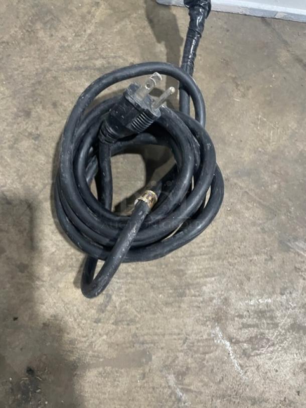 Coiled black power cord on concrete floor with a three-prong plug, part of a Dough Pro DP1100 pizza dough press machine.