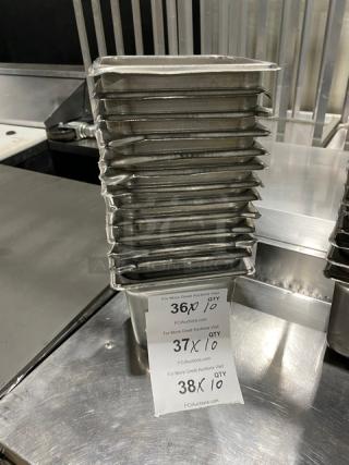 Commercial stainless steel hotel steam table pans stacked; auction tags indicate quantities and auction details.