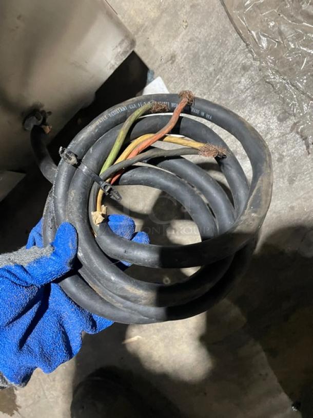 Coiled power cable held by gloved hand, condition appears used. Text on cable includes "made in USA." Likely part of Attias Magna Mixer.