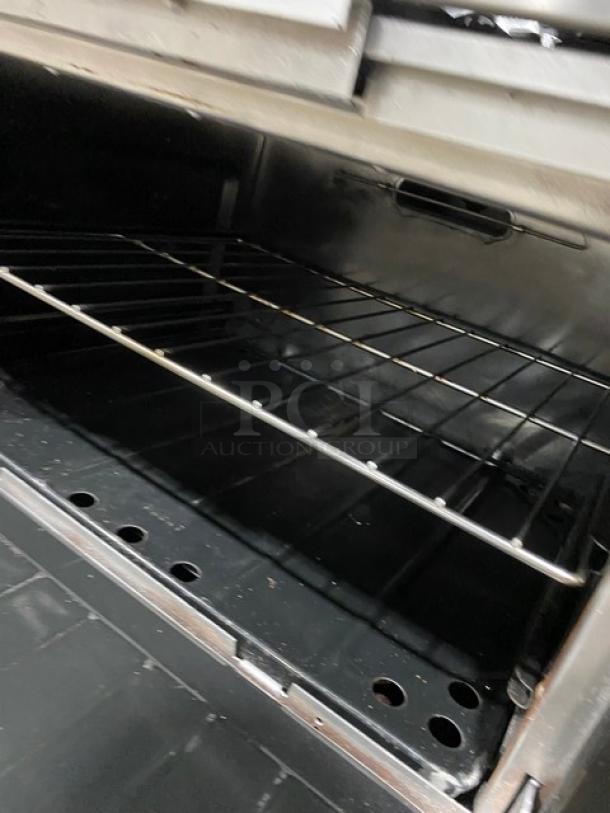 Garland commercial stainless steel range/oven, natural gas, 6 burners, with oven rack, backsplash, salamander shelf, on legs.