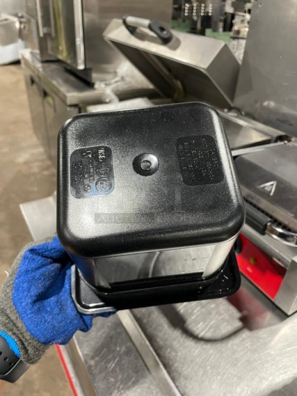 Cambro commercial black food pan, durable plastic, rectangular, visible product markings, held by gloved hand.