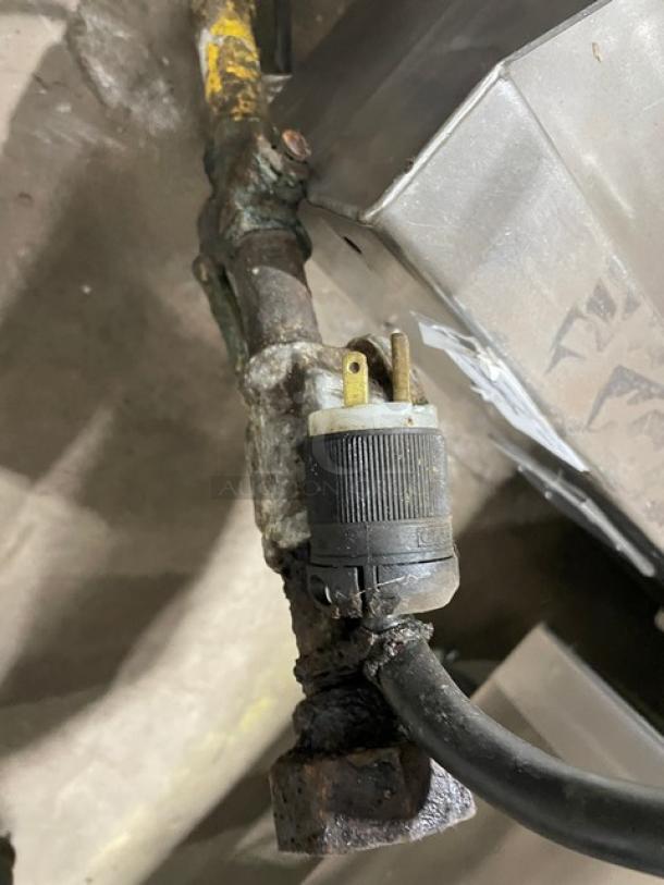 A worn and rusted metal connector attached to a pipe, featuring a two-prong plug.