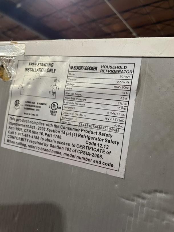 Black & Decker BCFA27 white refrigerator with upper freezer, poly-coated wired rack, model label and specifications visible.