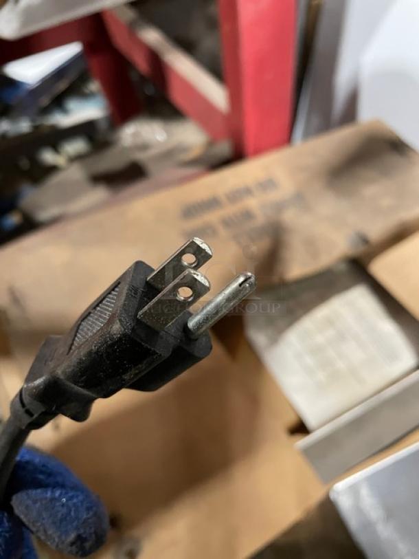 Close-up of a power plug belonging to a Black & Decker refrigerator with visible prongs. Background shows a cardboard box.