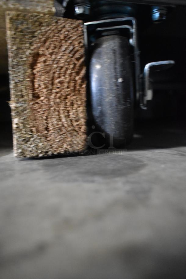 Commercial caster of Avantco 178GDC23HCB cooler, metal construction, on a wooden block, focus on caster detail.