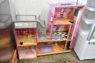 Colorful multi-level doll playhouse with furnished rooms, staircase, and vibrant decor. Auction tag labeled "75" visible.